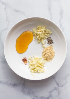 A white bowl with honey, ginger, sesame seeds, garlic, and other spices.