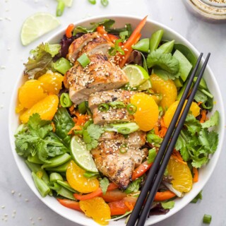 Asian Chicken Salad with Sesame Ginger Dressing that includes greens, mandarin oranges, limes, green onions, and sliced chicken