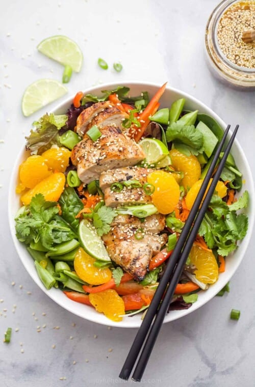 Asian Chicken Salad with Sesame Ginger Dressing that includes greens, mandarin oranges, limes, green onions, and sliced chicken