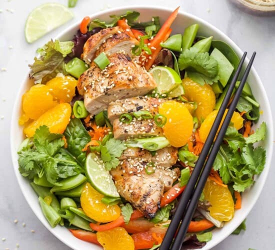 Asian Chicken Salad with Sesame Ginger Dressing that includes greens, mandarin oranges, limes, green onions, and sliced chicken