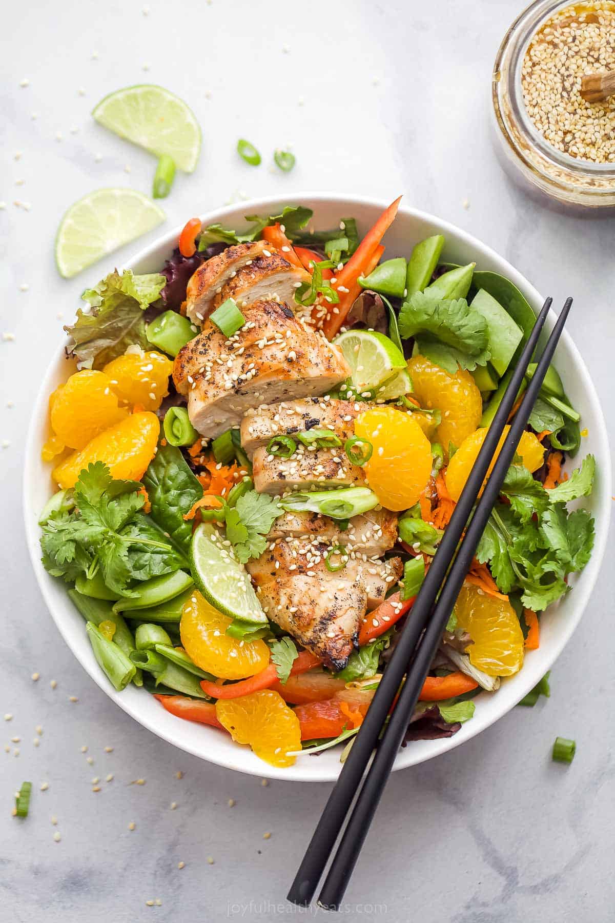 Asian Chicken Salad with Sesame Ginger Dressing that includes greens, mandarin oranges, limes, green onions, and sliced chicken