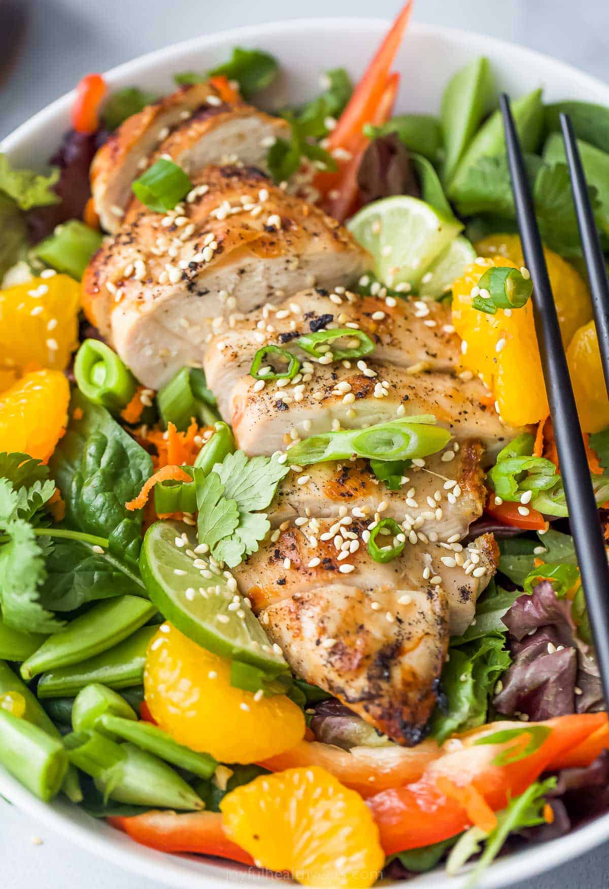 Asian Chicken Salad with Sesame Ginger Dressing that includes greens, mandarin oranges, limes, green onions, and sliced chicken