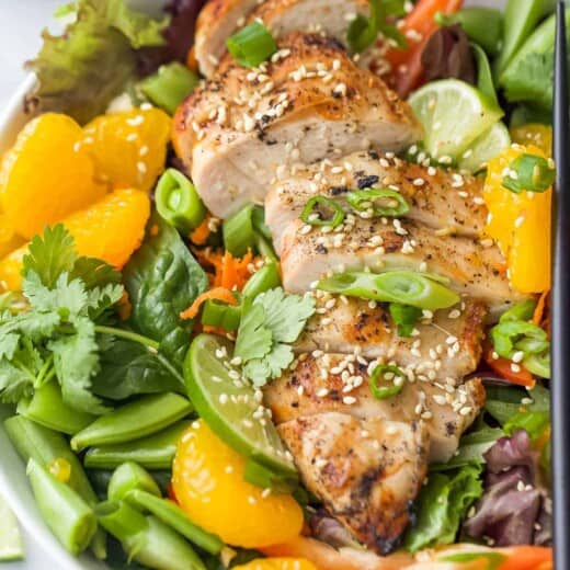 Asian Chicken Salad with Sesame Ginger Dressing that includes greens, mandarin oranges, limes, green onions, and sliced chicken