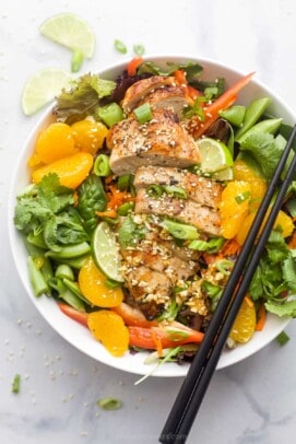 Asian Chicken Salad with Sesame Ginger Dressing that includes greens, mandarin oranges, limes, green onions, and sliced chicken