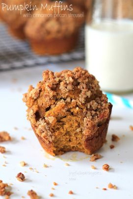 A pumpkin muffin with a bite taken out on a countertop with a glass of milk