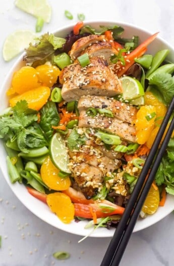 Asian Chicken Salad with Sesame Ginger Dressing that includes greens, mandarin oranges, limes, green onions, and sliced chicken