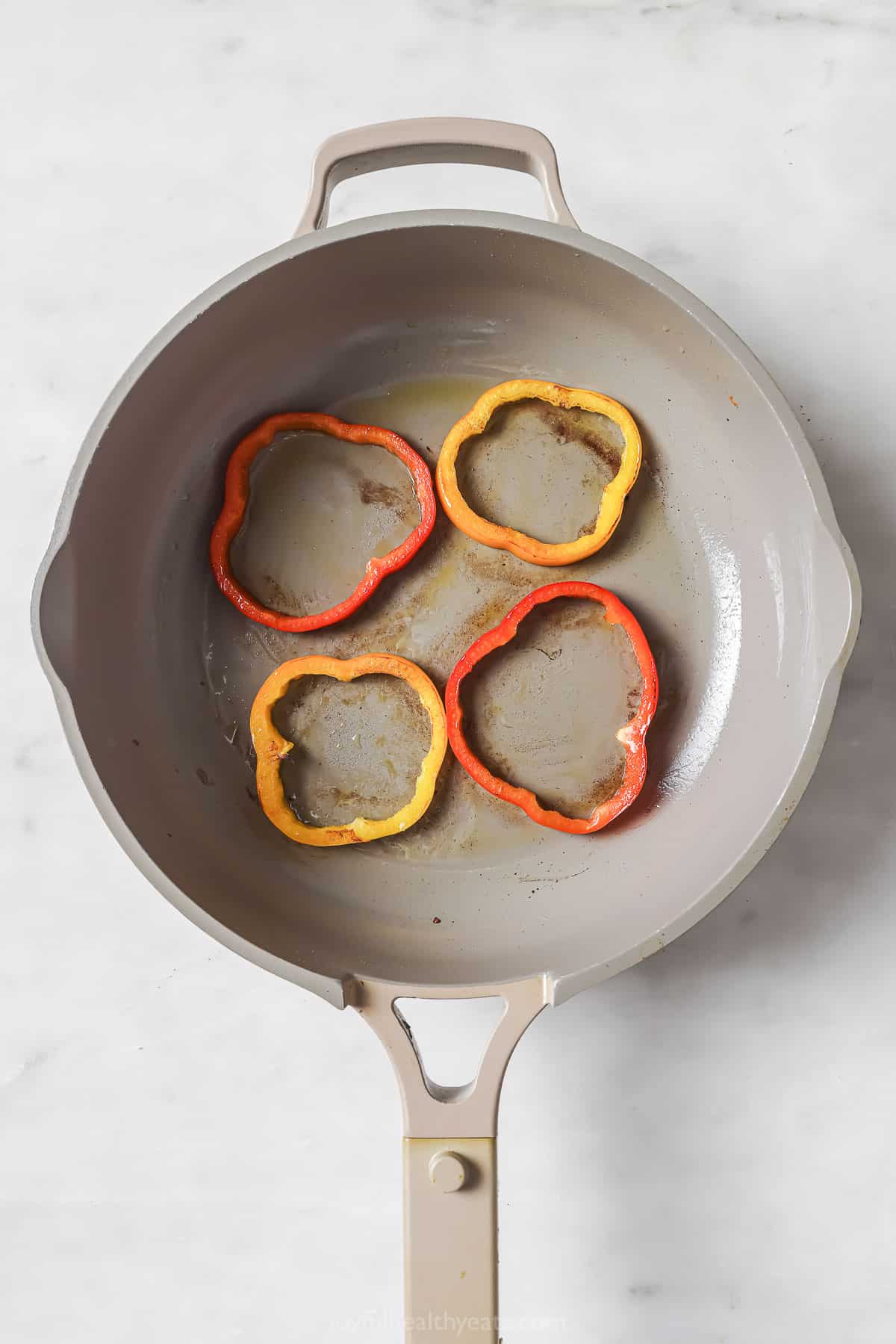 Large skillet with bell pepper rings sautéing. 