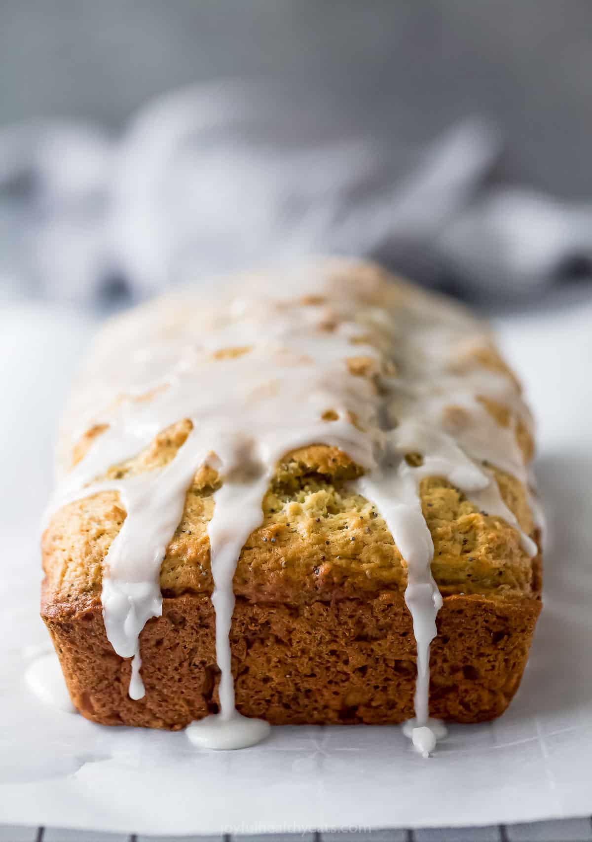 This lemon poppy seed bread is a zesty dessert-turned-breakfast packed with healthy ingredients like Greek yogurt for a guilt-free treat. Side shot of poppy seed bread with glaze dripping down the sides.