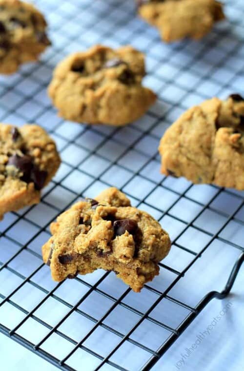 A cookie with a bite taken out of it on a wire, grid-patterned rack with other cookies