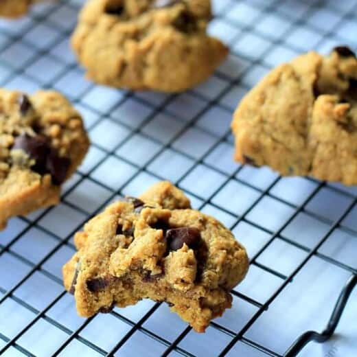 A cookie with a bite taken out of it on a wire, grid-patterned rack with other cookies