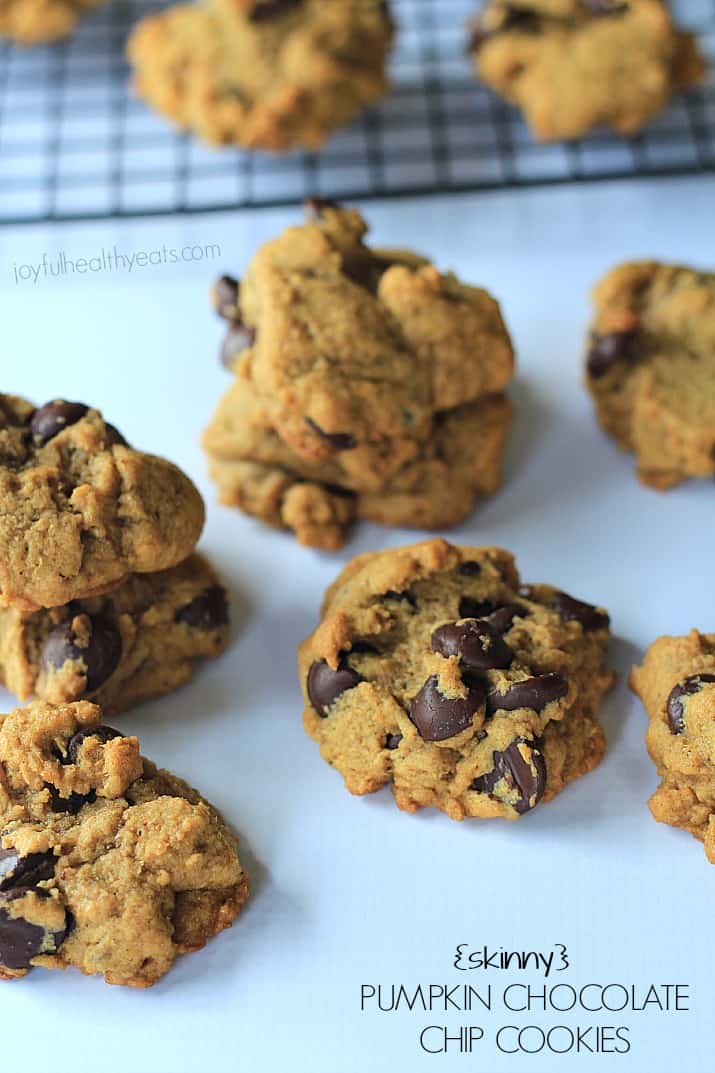 A bunch of chocolate chip cookies on a countertop with a cooling rack behind them