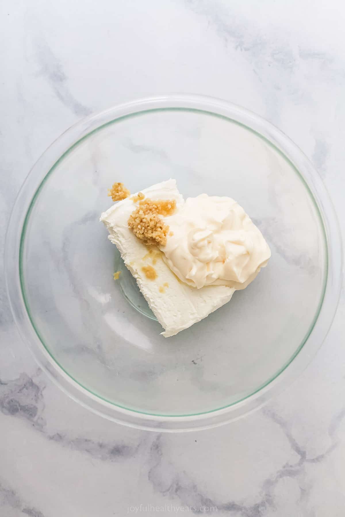 a glass bowl with cream cheese, garlic, and a scoop of mayonnaise