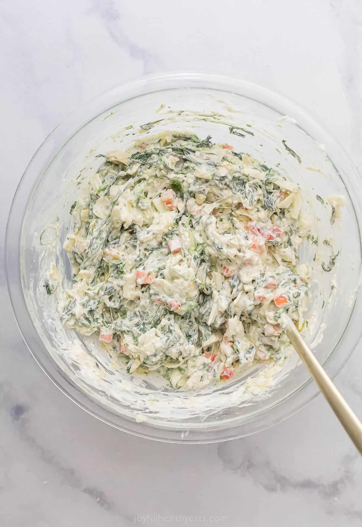 a creamy mixture of cream cheese, red peppers, and spinach in a bowl