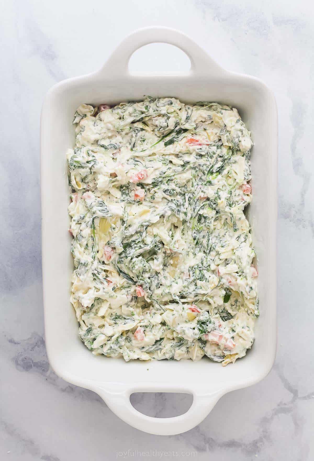 a casserole dish with uncooked crreamy spinach and artichoke dip