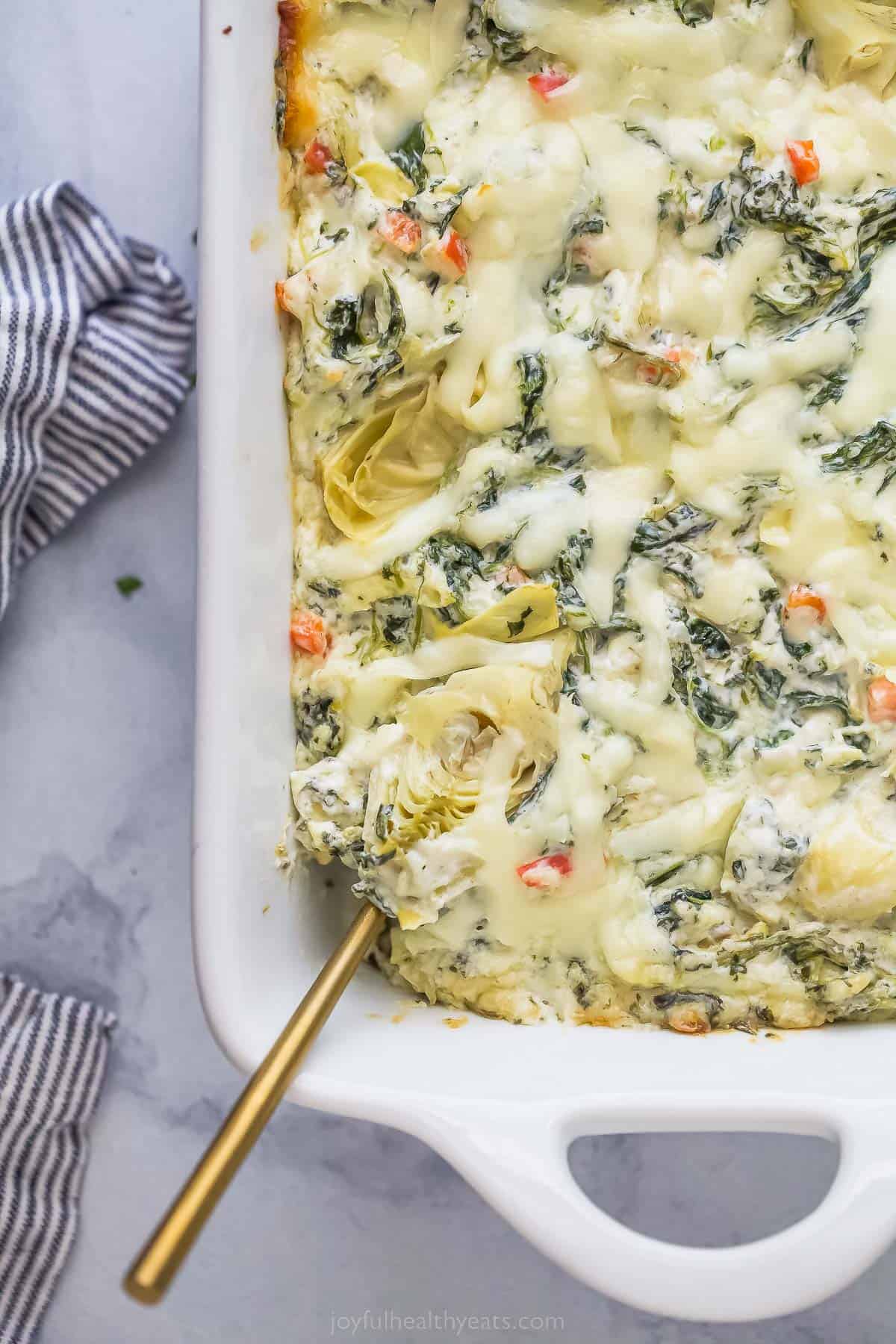 casserole dish with creamy spinach dip and a spoon in the side of the dip