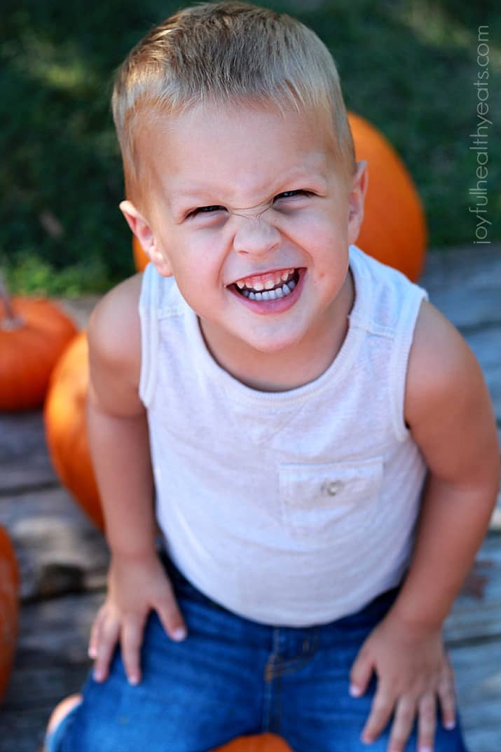 A smiling little boy sitting near pumpkins