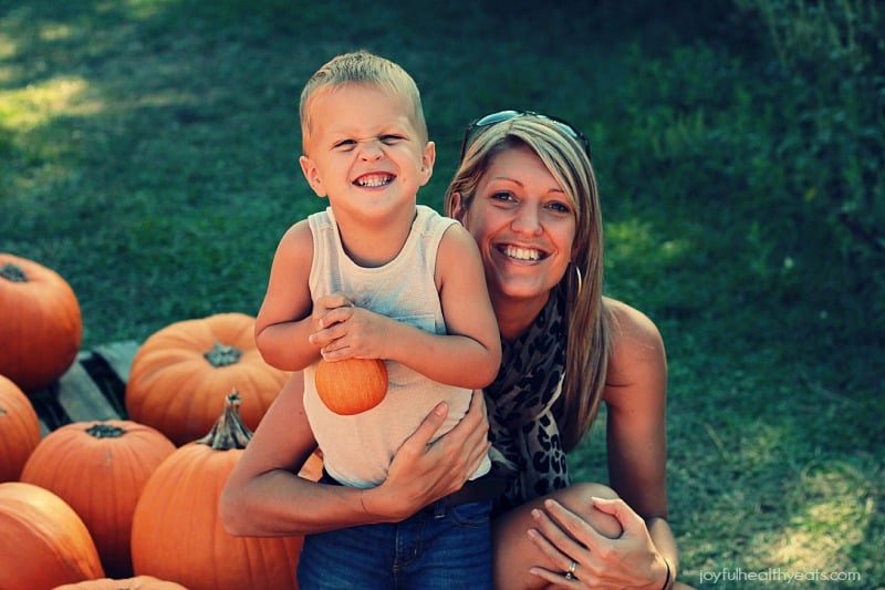 A boy and his mom next to several pumpkins