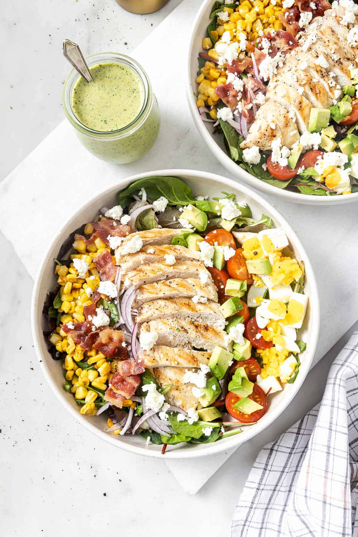This hearty chicken Cobb salad is jazzed up with Tex-Mex flavors, from avocado and queso fresco to a creamy and tangy poblano dressing! Chicken Cobb salad in two bowls with creamy poblano dressing in jar