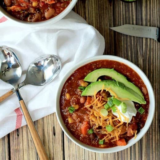 Two bowls of chili with avocado slices on top.