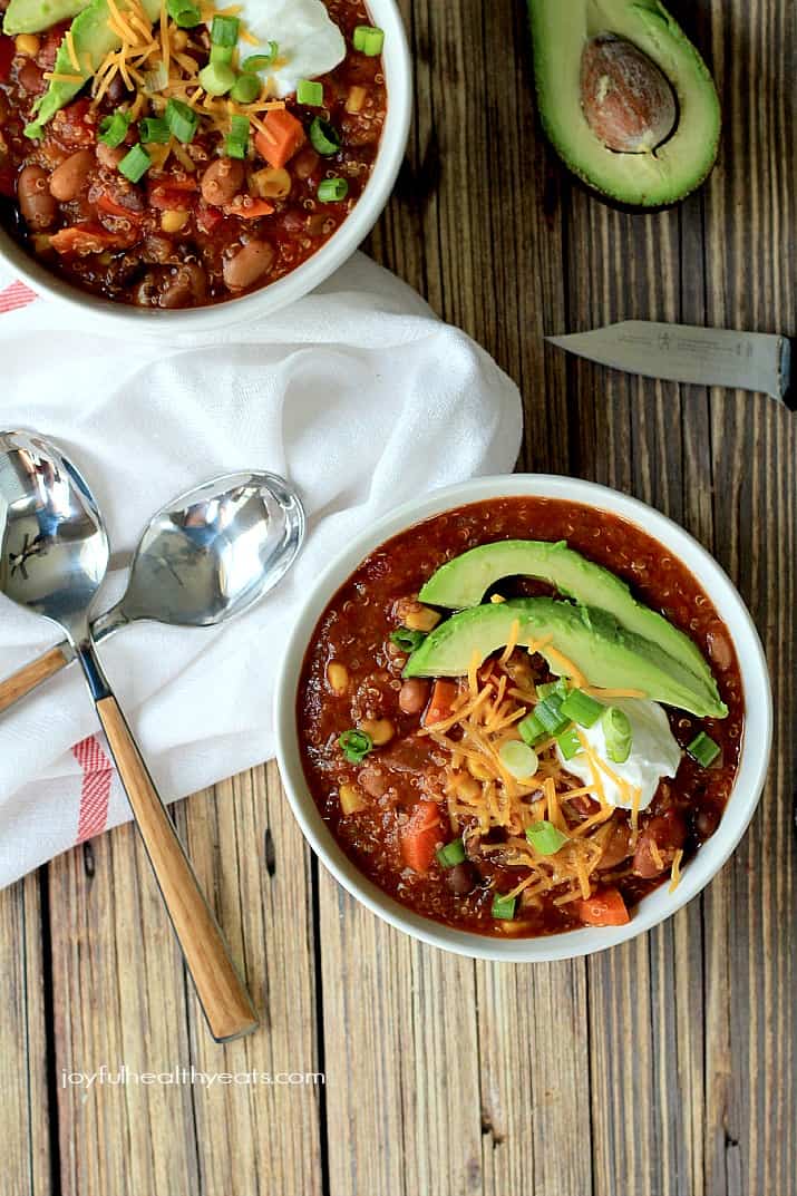 Top view of Quinoa Vegetarian Chili in bowls topped with scallions, shredded cheese, sour cream, and sliced avocado