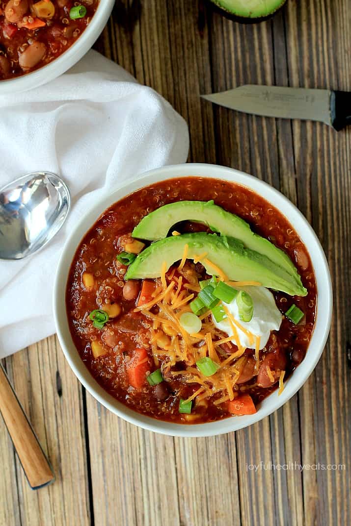 Top view of Quinoa Vegetarian Chili in a bowl topped with scallions, shredded cheese, sour cream, and sliced avocado