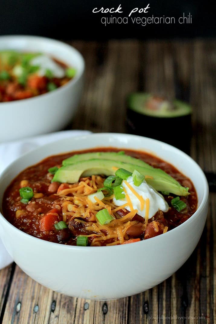 Crock Pot Quinoa Vegetarian Chili in a bowl topped with shredded cheese, sour cream, sliced avocado and scallions