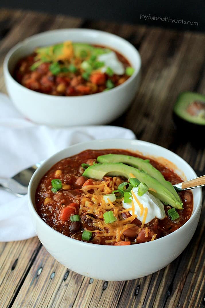 Two bowls of Quinoa Vegetarian Chili topped with scallions, shredded cheese, sour cream, and sliced avocado