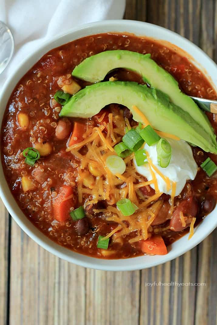 Close up view of a bowl of Quinoa Vegetarian Chili topped with scallions, shredded cheese, sour cream, and sliced avocado