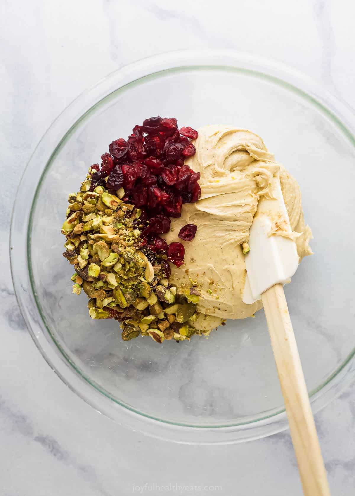 Dried cranberries and chopped pistachios in a bowl with the dough and a rubber spatula