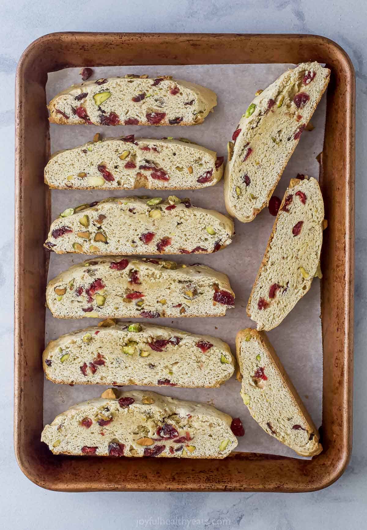 Nine pieces of partially-baked biscotti on a parchment-lined baking sheet