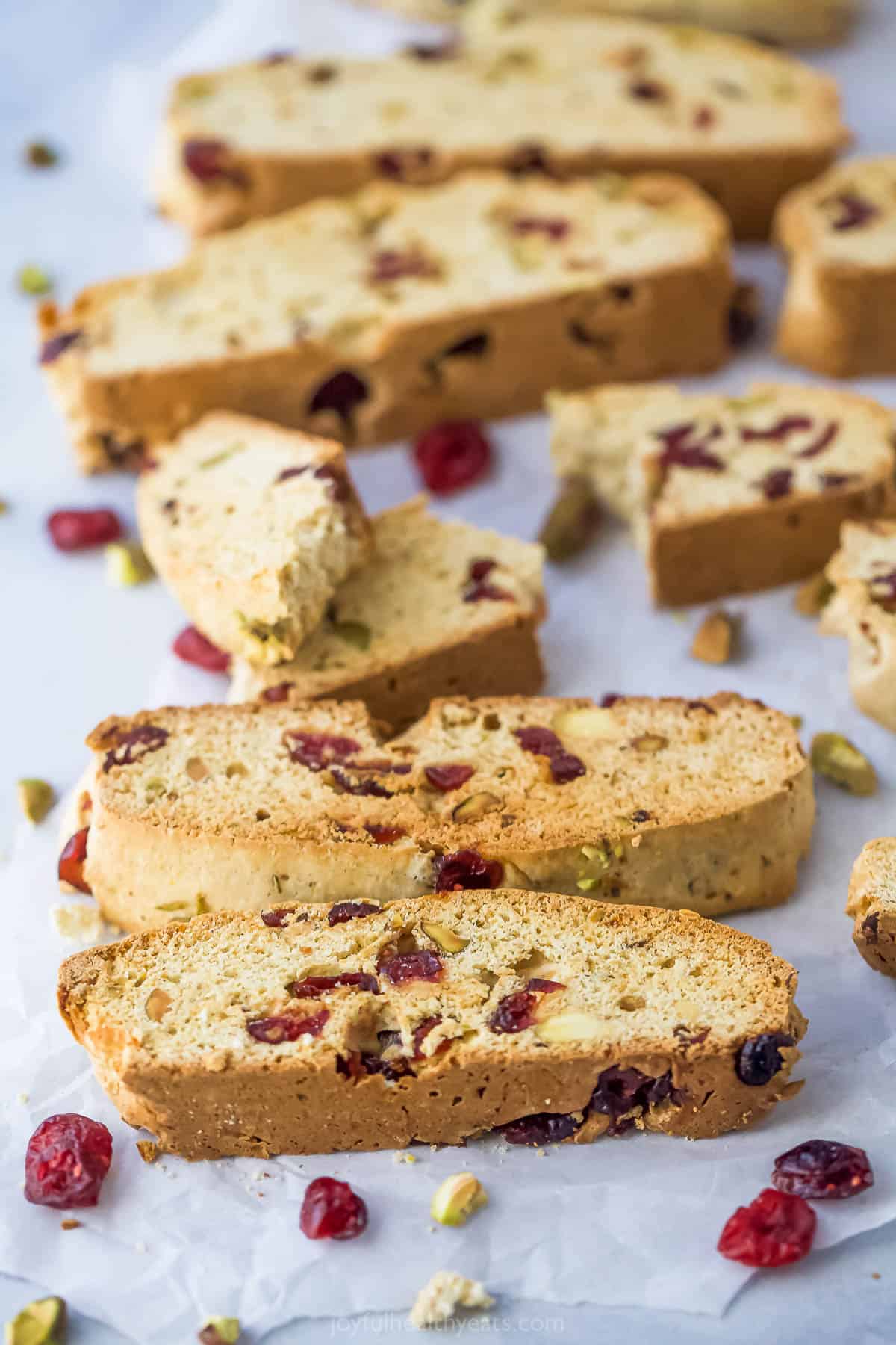 Cranberry pistachio biscotti cookies on top of a sheet of parchment paper with loose craisins and pistachios