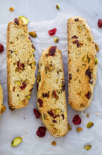 Three cranberry pistachio biscotti cookies lined up on a sheet of parchment paper