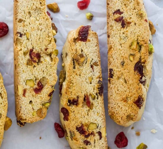 Three cranberry pistachio biscotti cookies lined up on a sheet of parchment paper