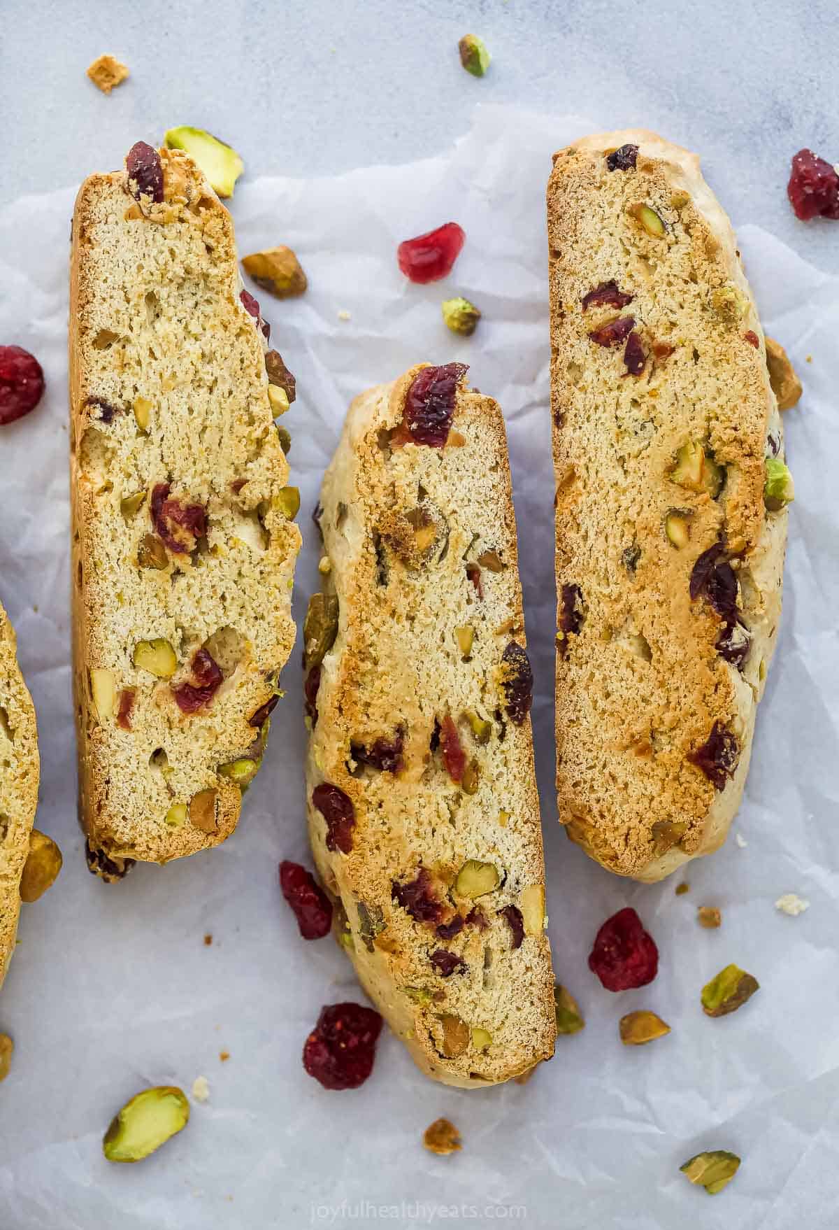 Three cranberry pistachio biscotti cookies lined up on a sheet of parchment paper