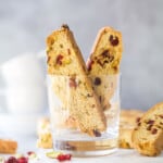 Two pieces of biscotti inside of a glass cup on top of a cutting board