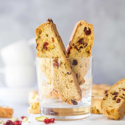 Two pieces of biscotti inside of a glass cup on top of a cutting board