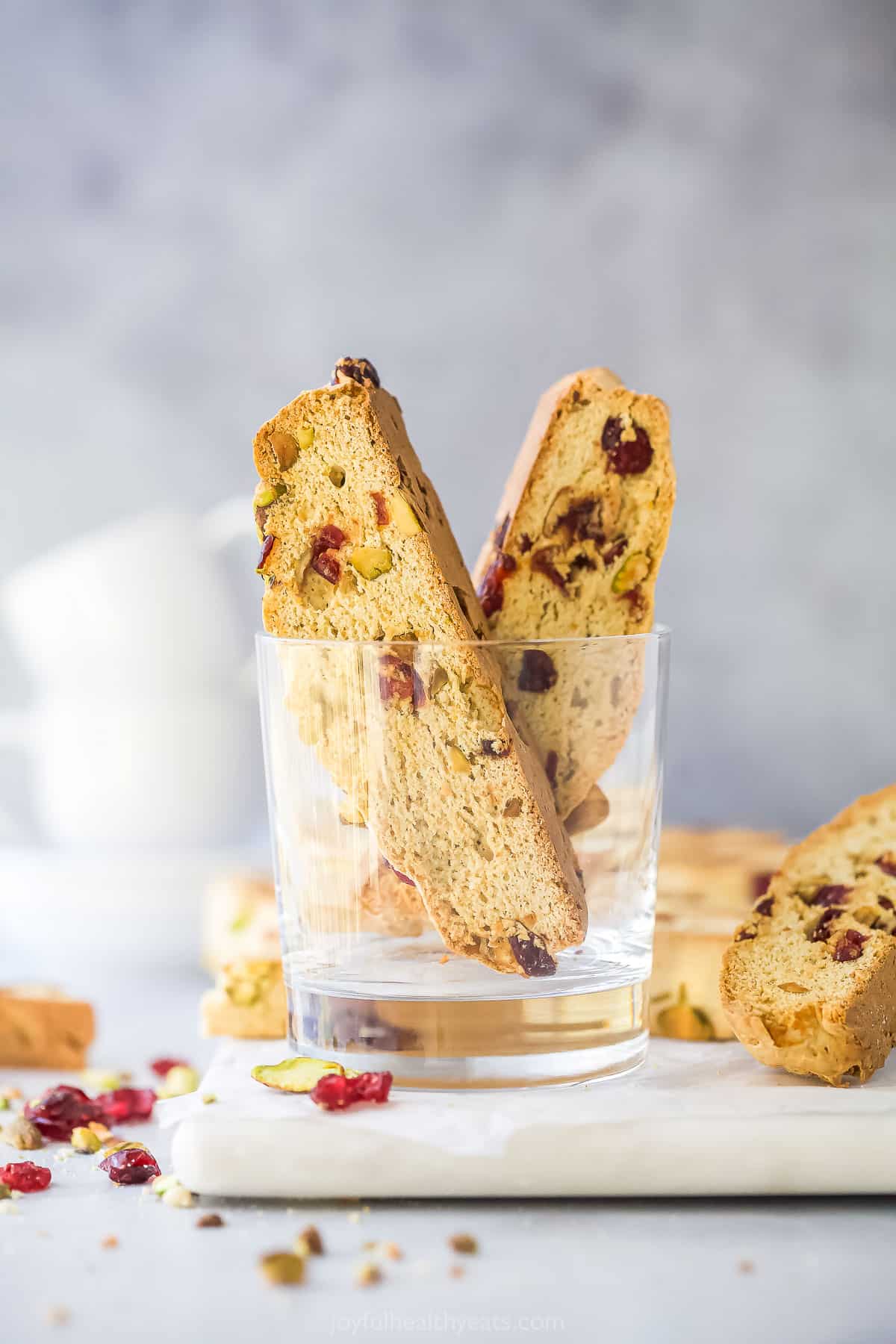 Two pieces of biscotti inside of a glass cup on top of a cutting board