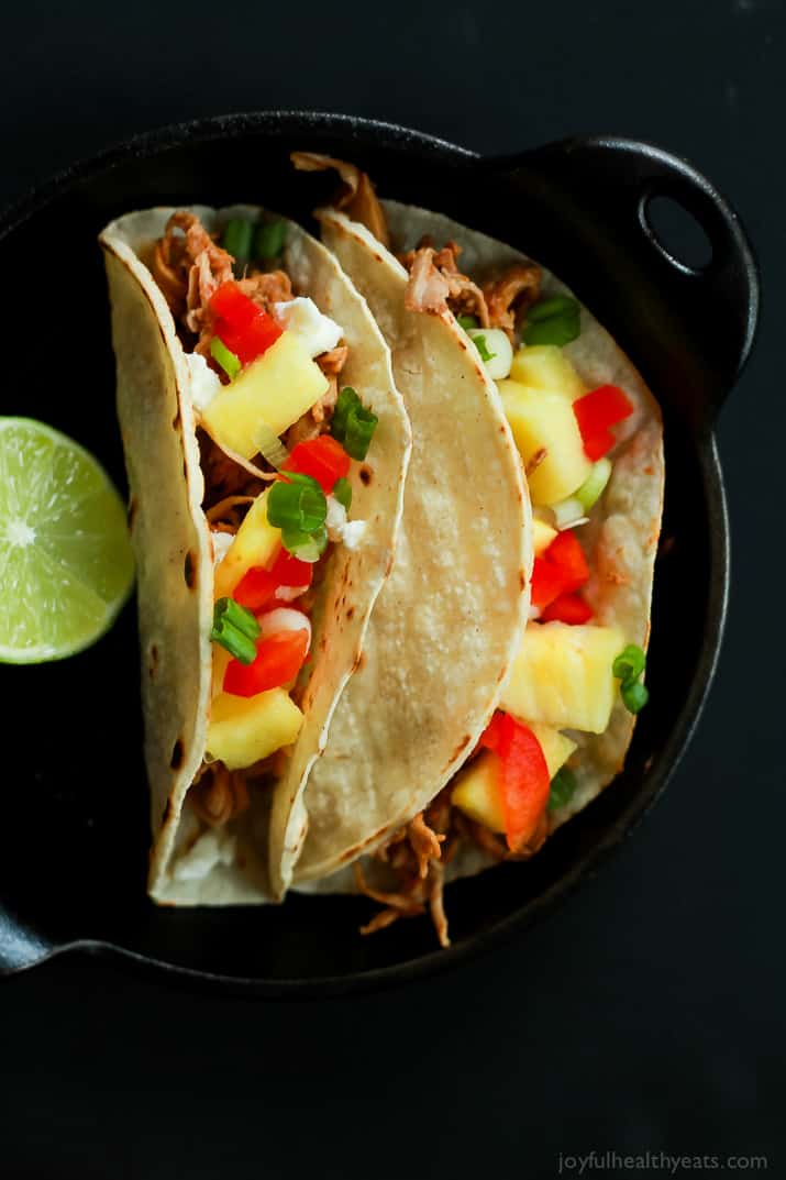 Top view of two Hawaiian Pork Tacos filled with sweet pulled pork, fresh pineapple, red peppers, and goat cheese