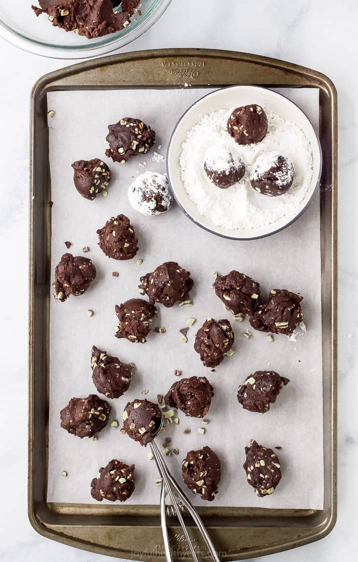 chocolate cookies being rolled in powdered sugar