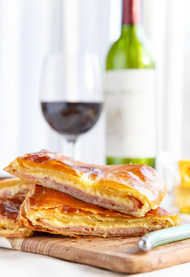 Two Ham and Cheese Puff Pastry Squares in Front of a Glass and Bottle of Wine