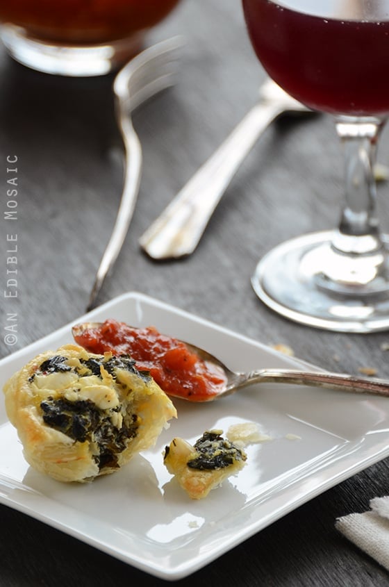 A Spanakopita Puff on a Square Plate Next to a Glass of Wine