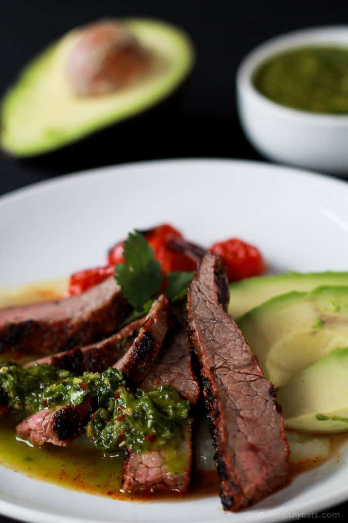 Close-up of sliced Chili Rubbed Flank Steak on a plate served with fresh chimichurri sauce and avocado