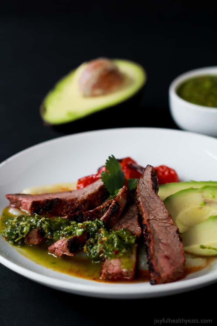 Slices of Chili Rubbed Flank Steak on a plate served with fresh chimichurri sauce and avocado
