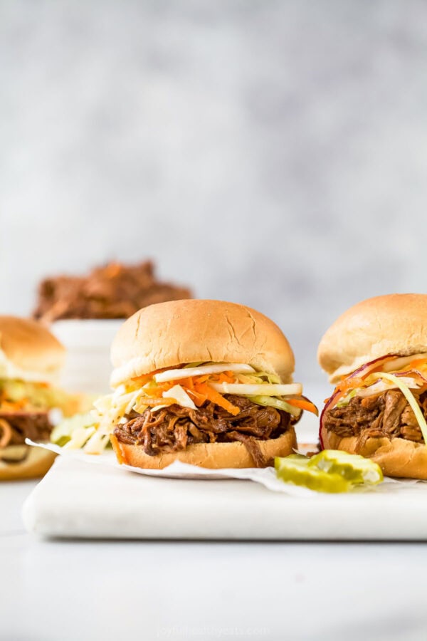 Pulled pork sliders on marble board with pickles.