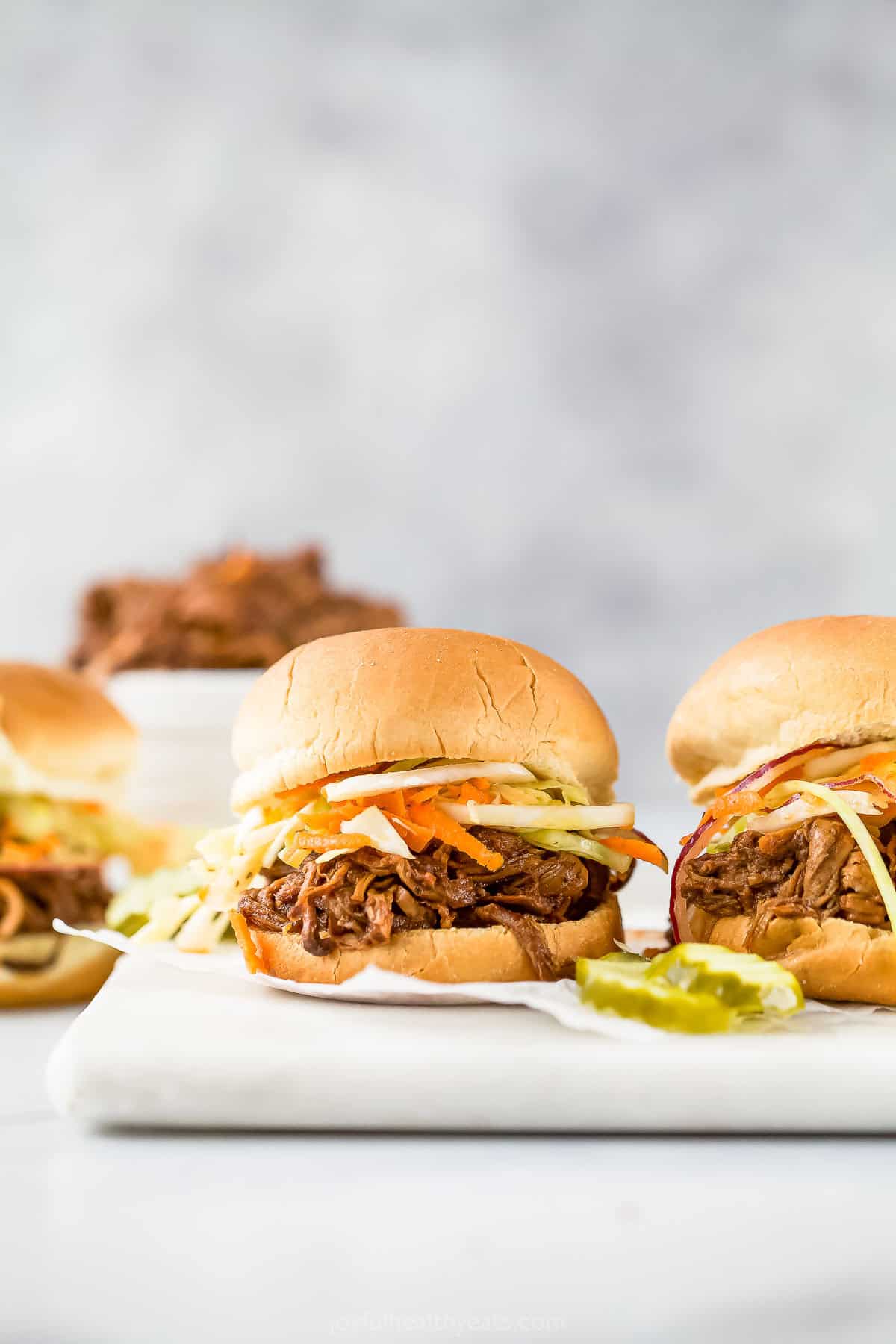 Pulled pork sliders on marble board with pickles.