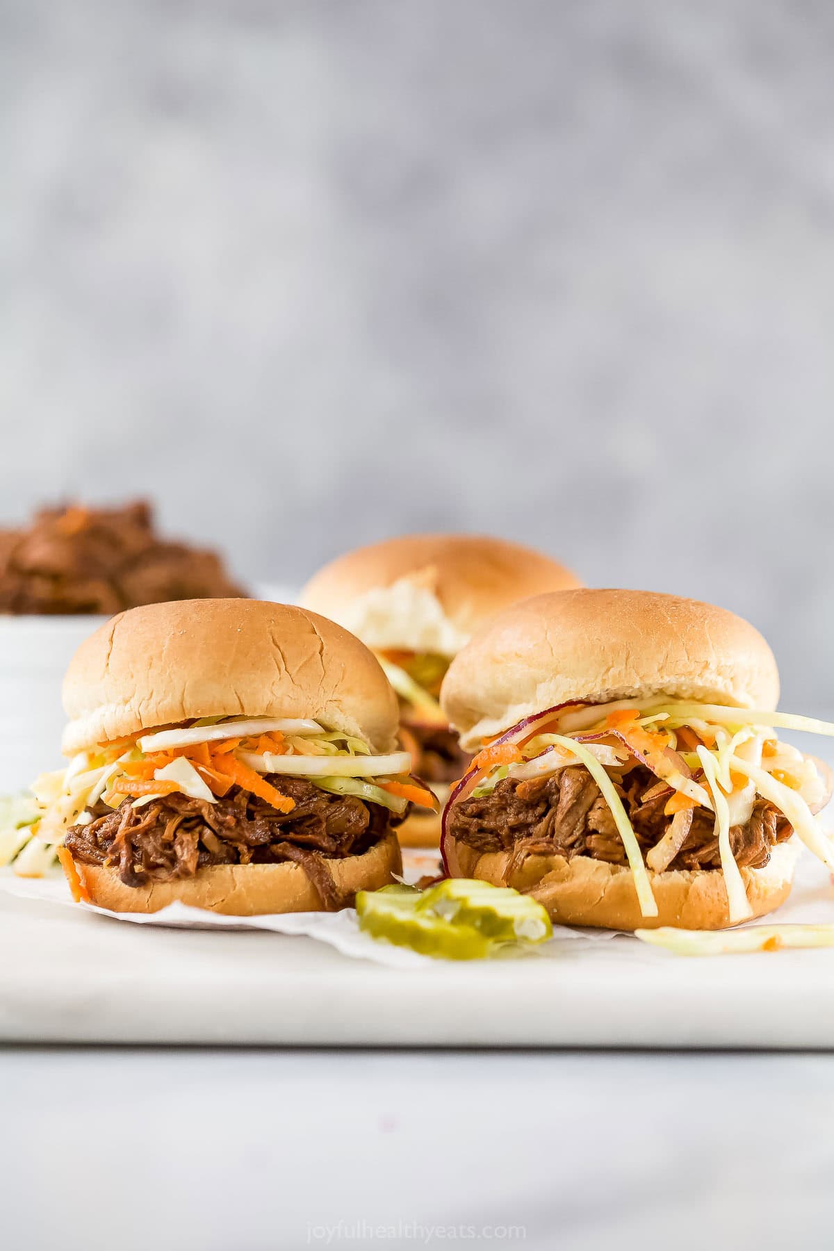 Pulled pork sliders on marble board with pickle slices.