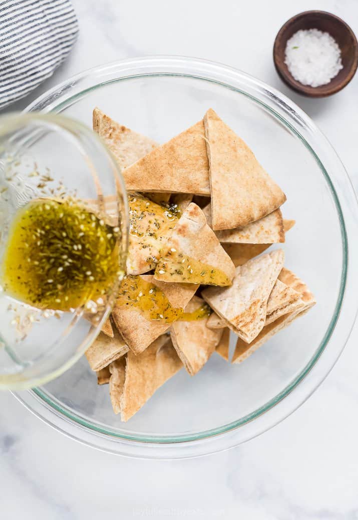 pouring herb olive oil mixture over pita chips