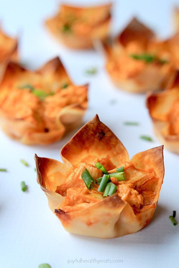 A mini Buffalo Chicken Wonton Cup with chives on a white surface