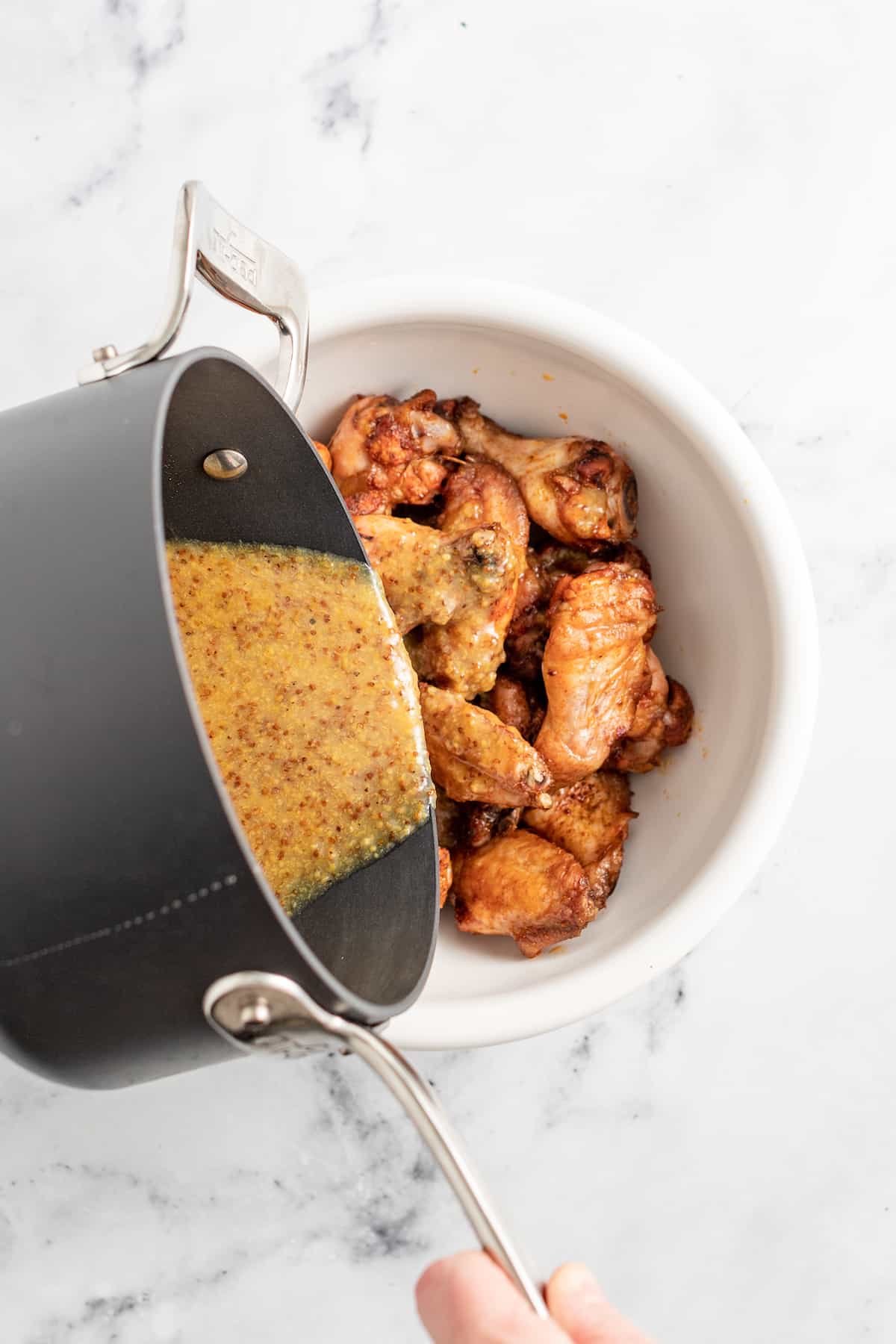 pouring sauce over a bowl of chicken wings