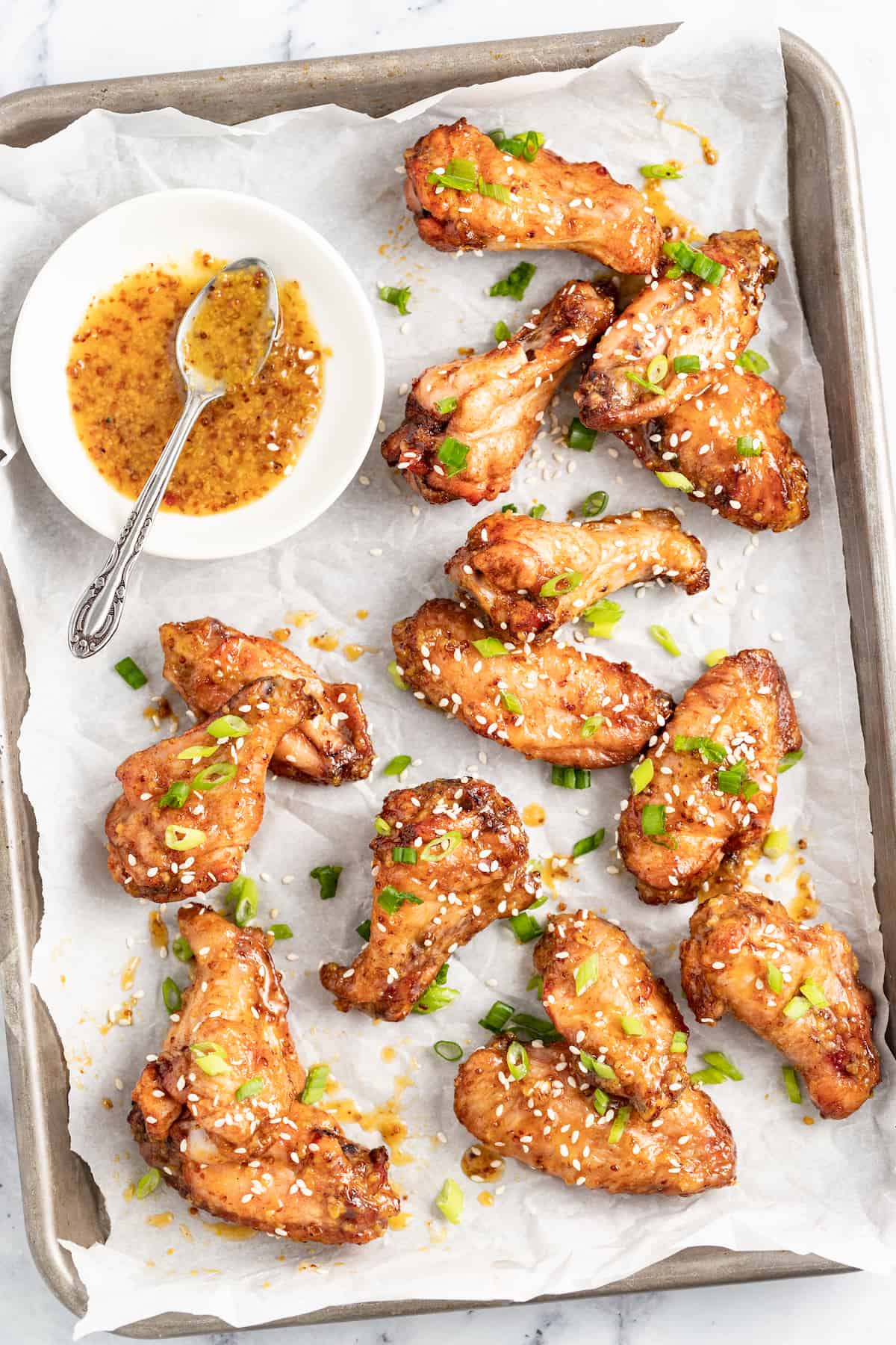 baked chicken wings on a lined sheet tray with sesame seed and herb garnish with a side of honey mustard sauce